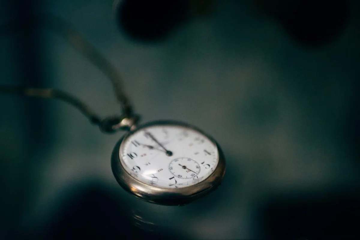 Reloj de bolsillo plateado con cadena sobre una superficie oscura, con el fondo desenfocado
