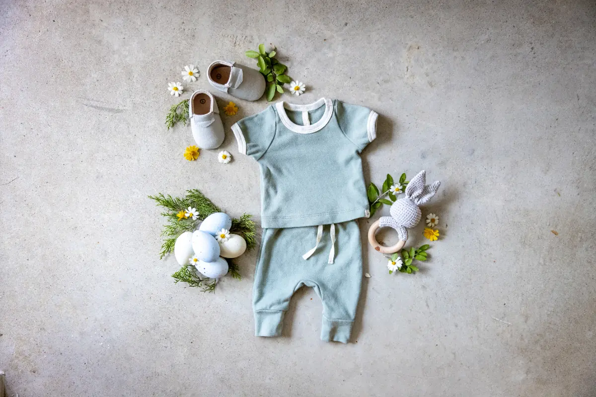 Conjunto de ropa de bebé, zapatitos, un sonajero y pequeñas flores colocados sobre un suelo de cemento gris