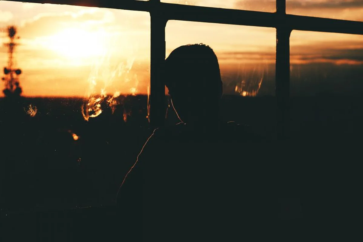 Silueta de una persona mirando por la ventana al atardecer