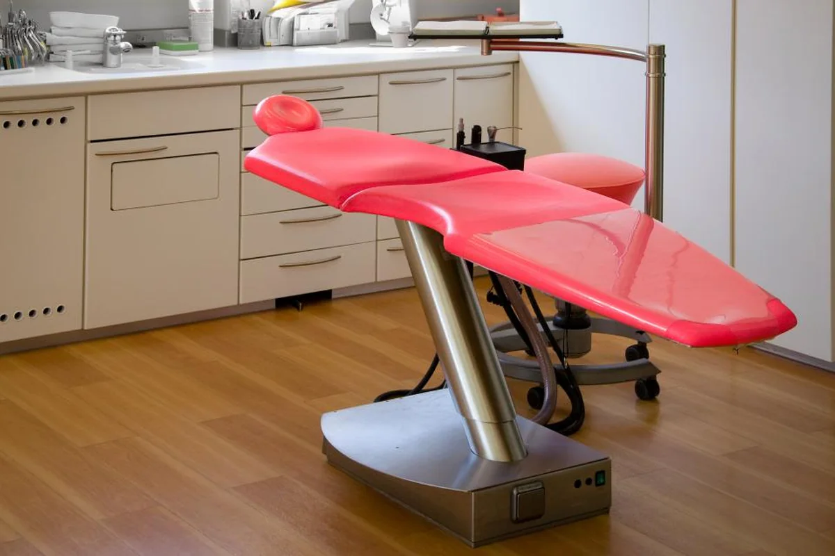 Sillón de consulta de color rojo, vacío, en una clínica con muebles blancos y suelo de madera