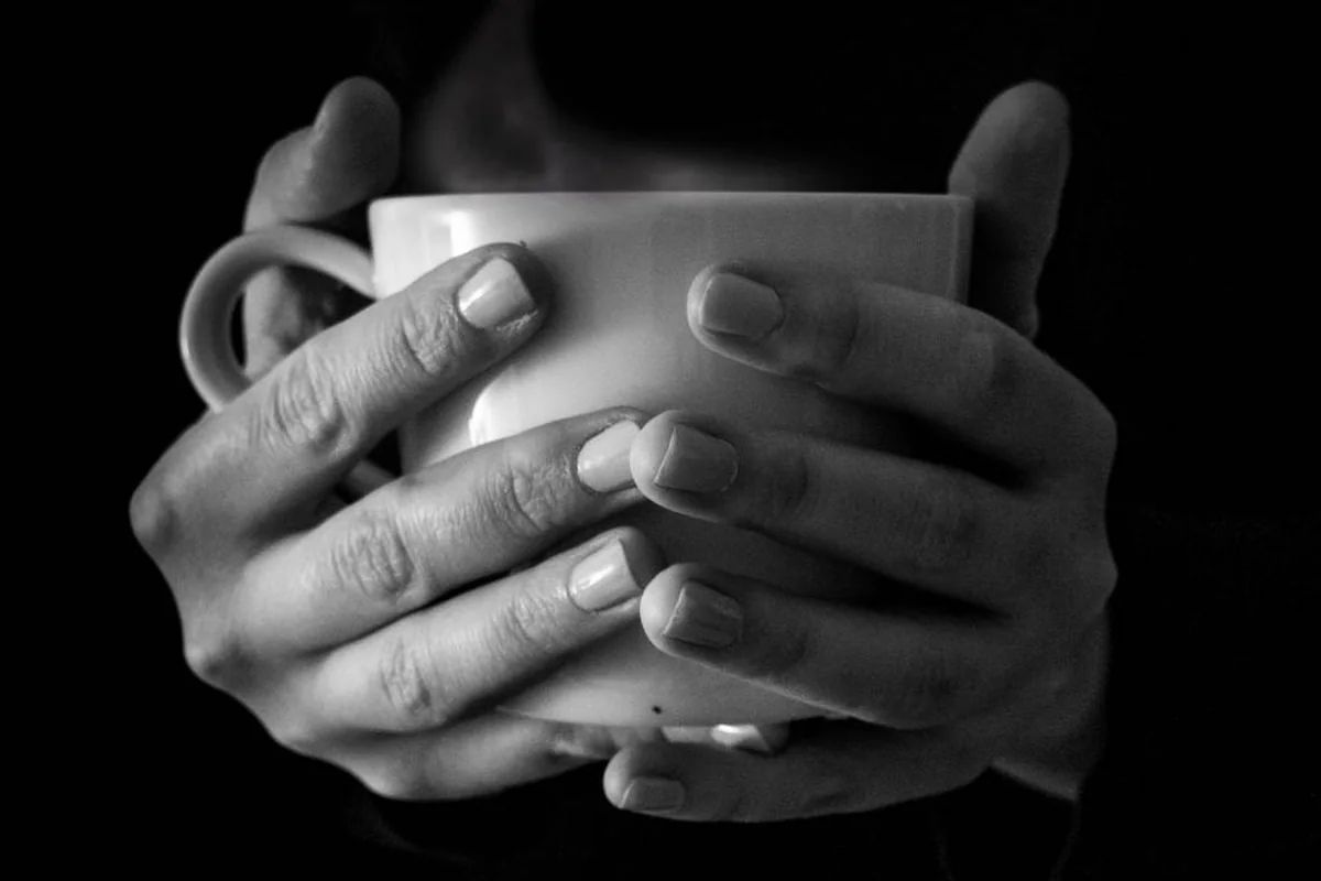 Manos sosteniendo una taza caliente en un ambiente hogareño tenue