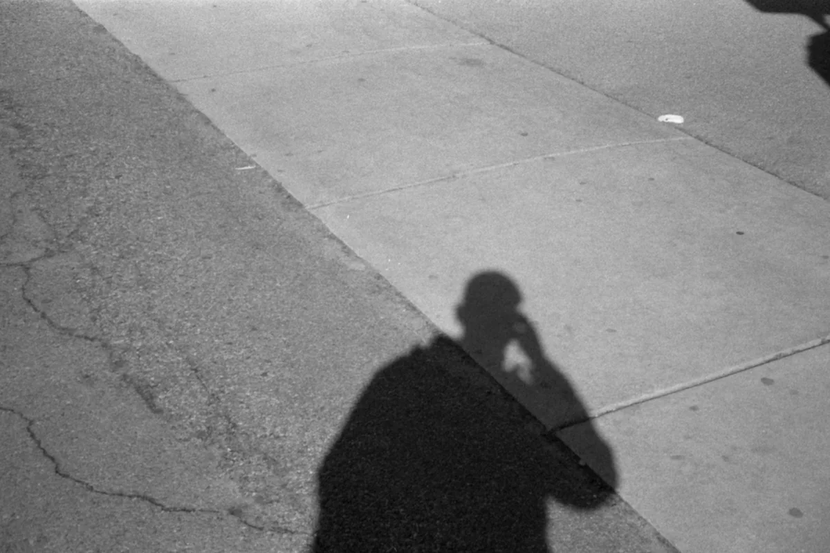 Fotografía en blanco y negro de la sombra de una persona proyectada sobre una acera agrietada