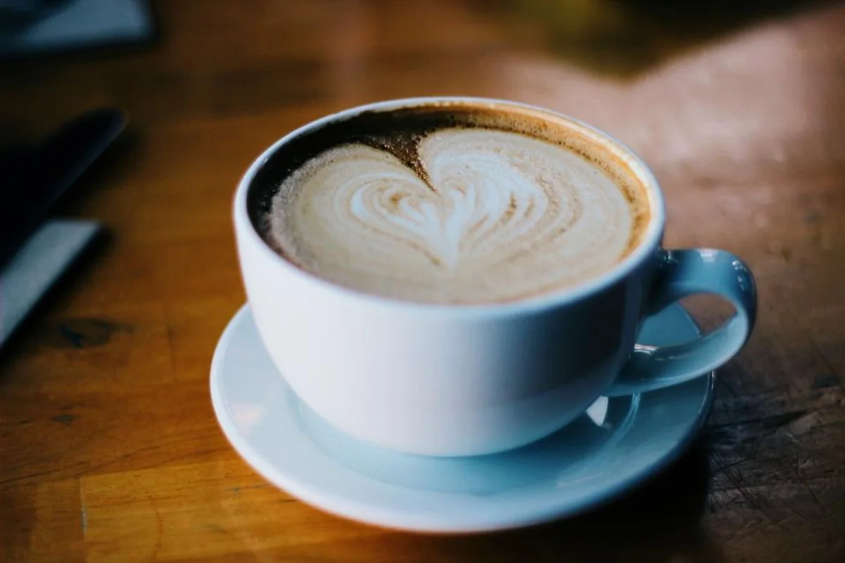 Taza blanca de capuchino con un corazón dibujado en la espuma sobre una mesa de madera