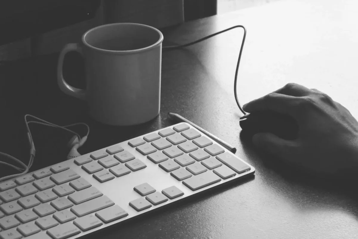 Taza en blanco y negro sobre una mesa junto a un teclado mientras una mano descansa sobre el ratón