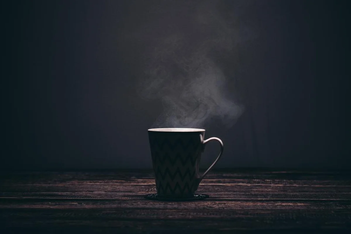 Taza de la que sale vapor sobre una mesa, con un fondo oscuro y vacío