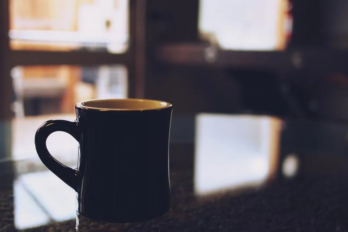 Taza oscura sola sobre una mesa brillante, con una ventana desenfocada reflejada al fondo