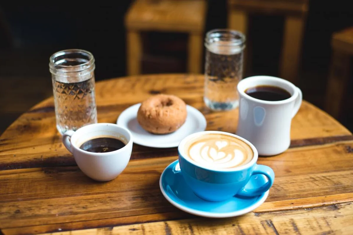 Varias tazas de café, un rosco en un plato y dos vasos de agua sobre una mesa redonda de madera