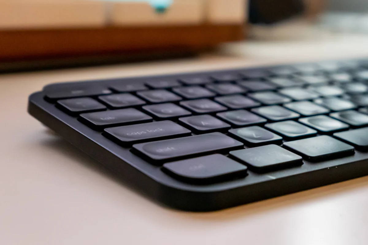 Teclado negro visto en ángulo sobre una mesa clara, con el fondo desenfocado