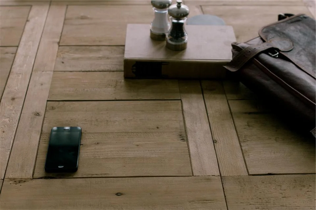 Teléfono móvil apagado sobre una mesa de tablones de madera, junto a un maletín de cuero oscuro, un libro y unos saleros