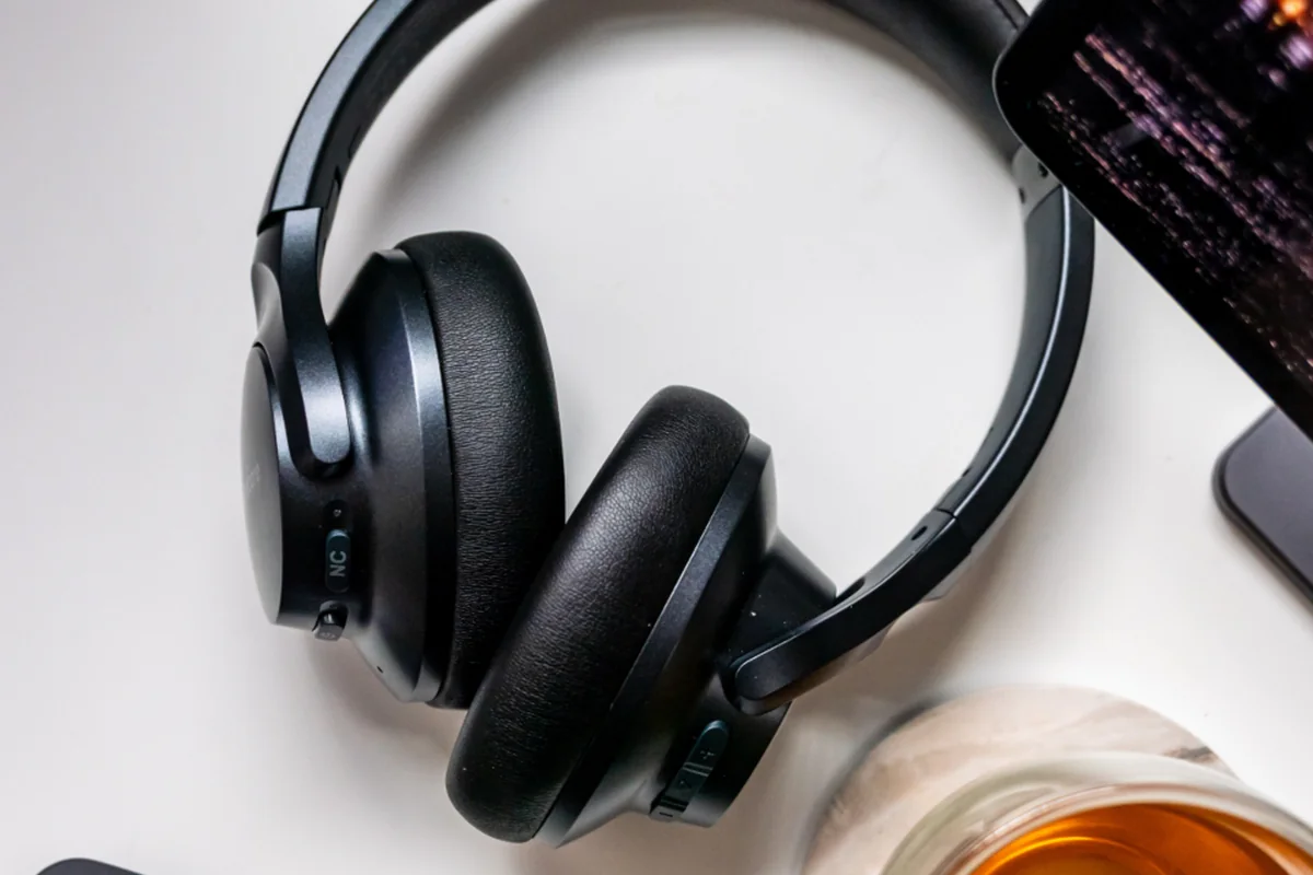 Auriculares de diadema negros sobre una mesa blanca junto a un teléfono móvil