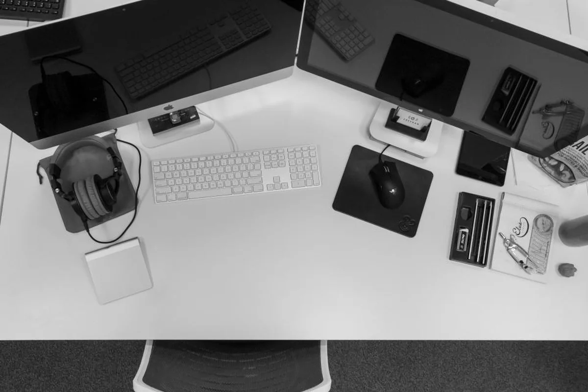 Escritorio en blanco y negro visto desde arriba con dos pantallas, teclado, ratón y auriculares
