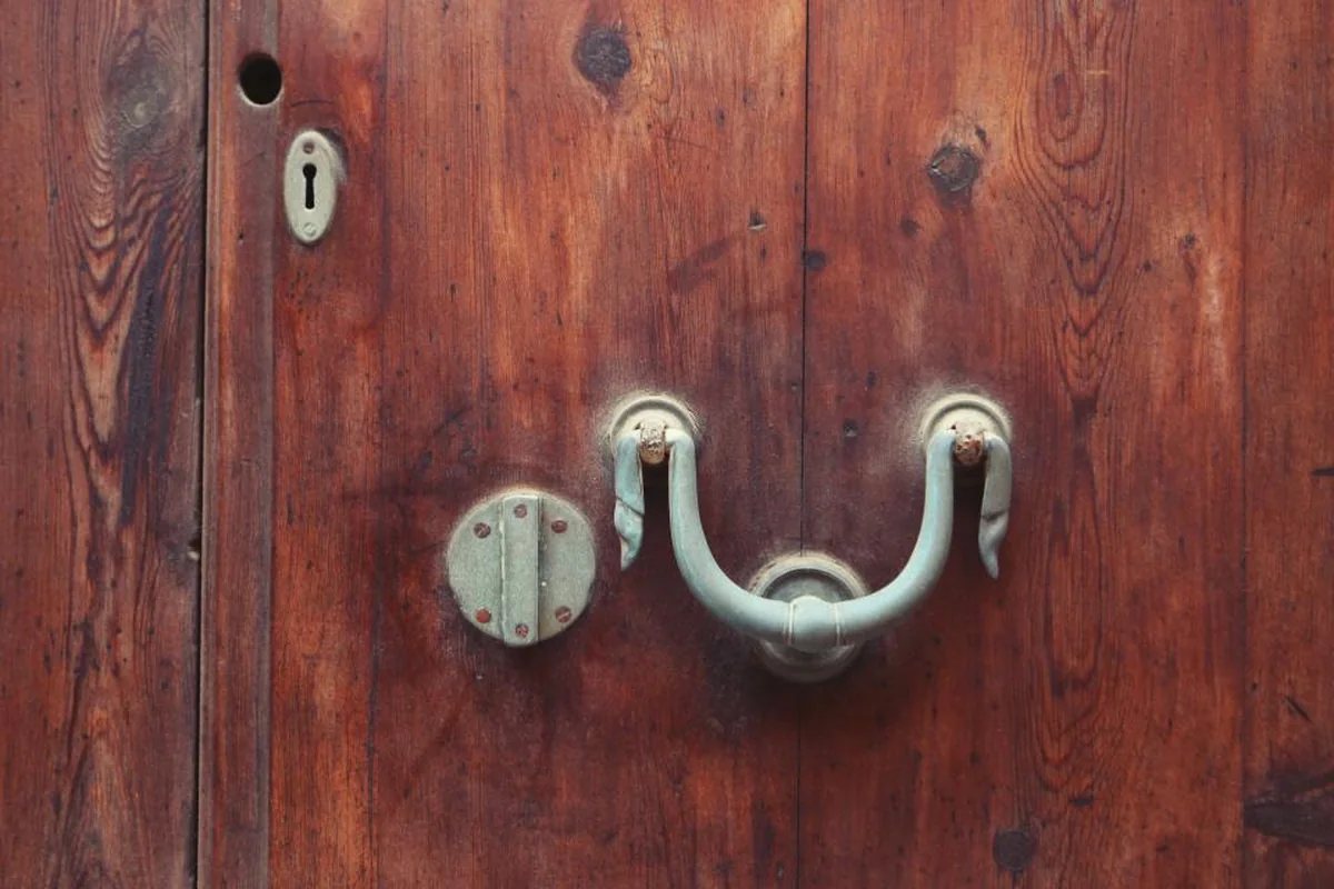 Una puerta de madera envejecida con un tirador metálico verde claro y una cerradura antigua