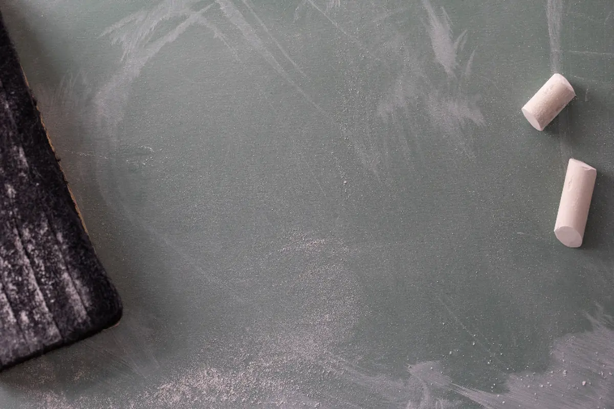 Dos tizas blancas y un borrador sobre una pizarra verde con restos de tiza borrada