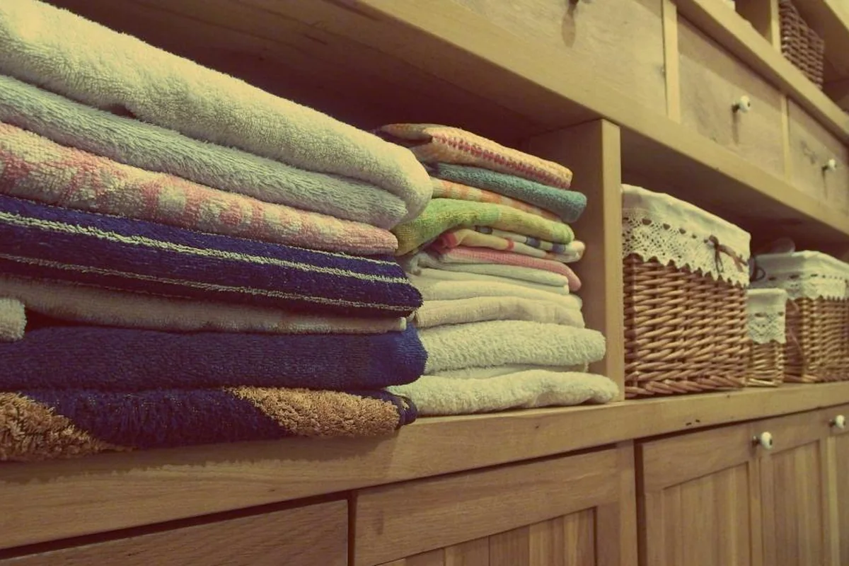 Toallas de distintos colores dobladas y apiladas en una estantería de madera junto a cestas de mimbre