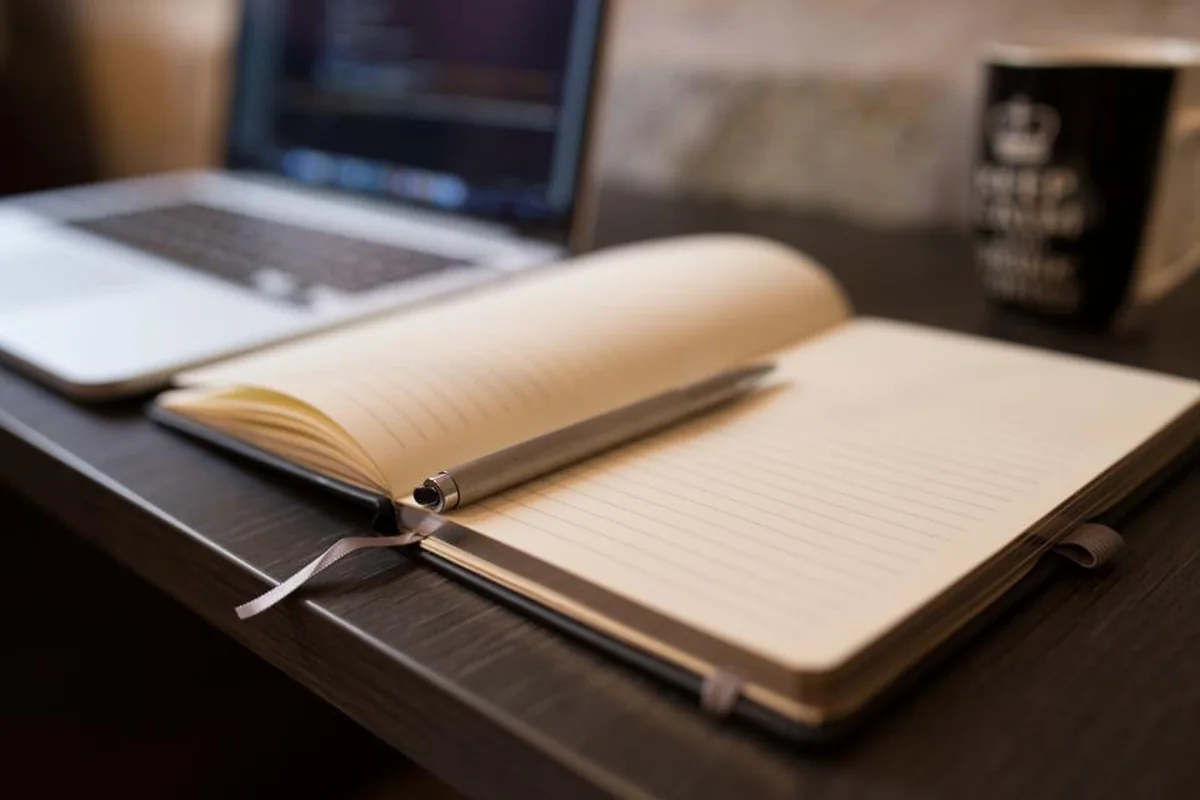 Portátil abierto junto a un cuaderno y una taza sobre una mesa de madera
