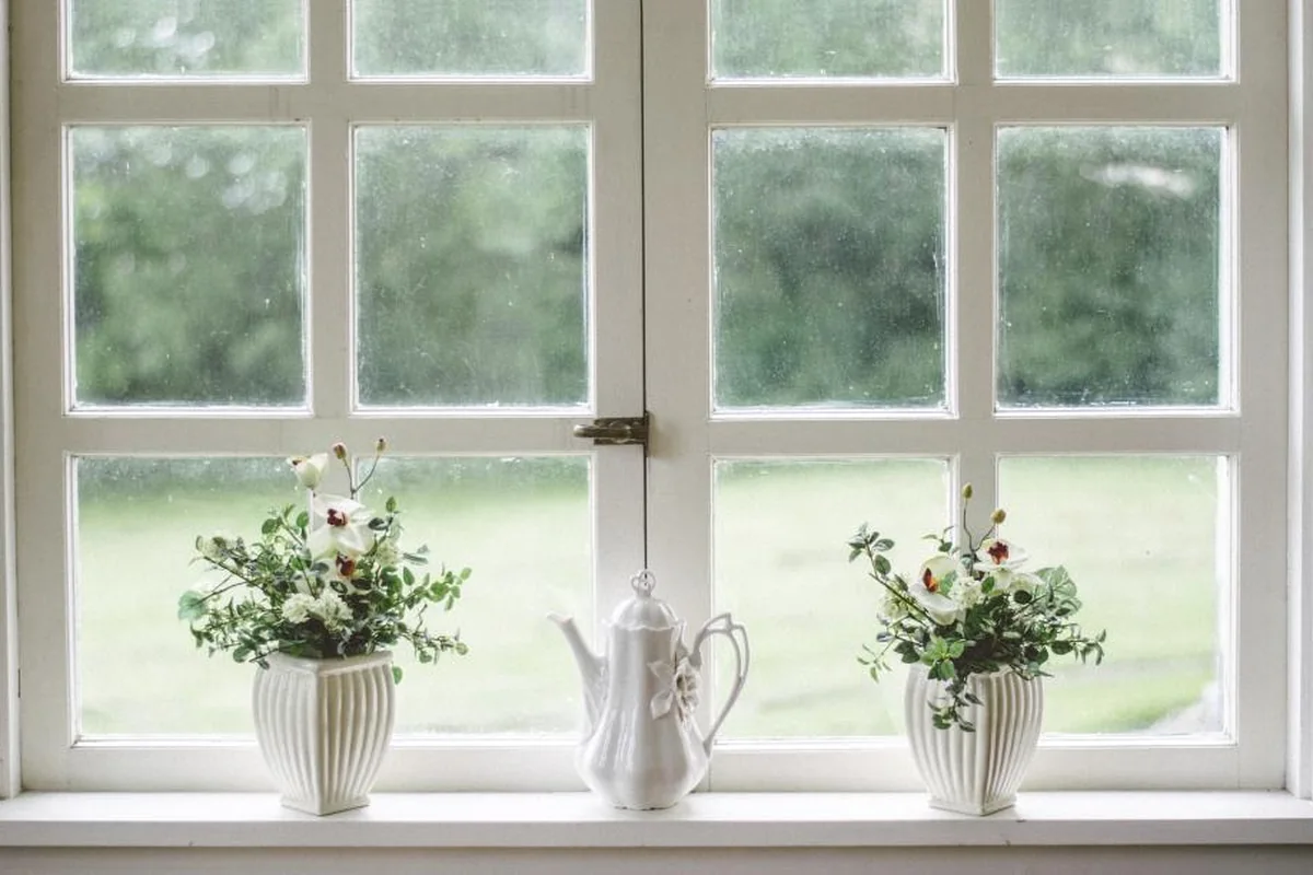 Ventana blanca con una jarra y flores sobre el alféizar