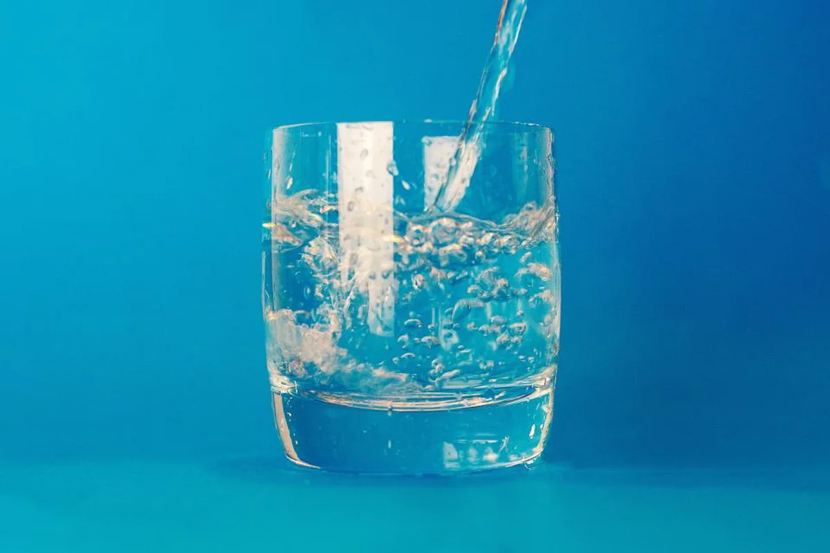Vaso de cristal llenándose de agua sobre un fondo azul intenso