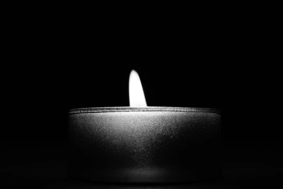 Pequeña vela encendida dentro de un recipiente metálico sobre un fondo completamente negro, en blanco y negro