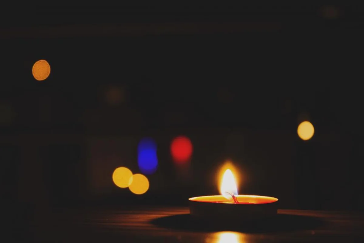 Pequeña vela encendida sobre una mesa en una habitación a oscuras con luces desenfocadas al fondo