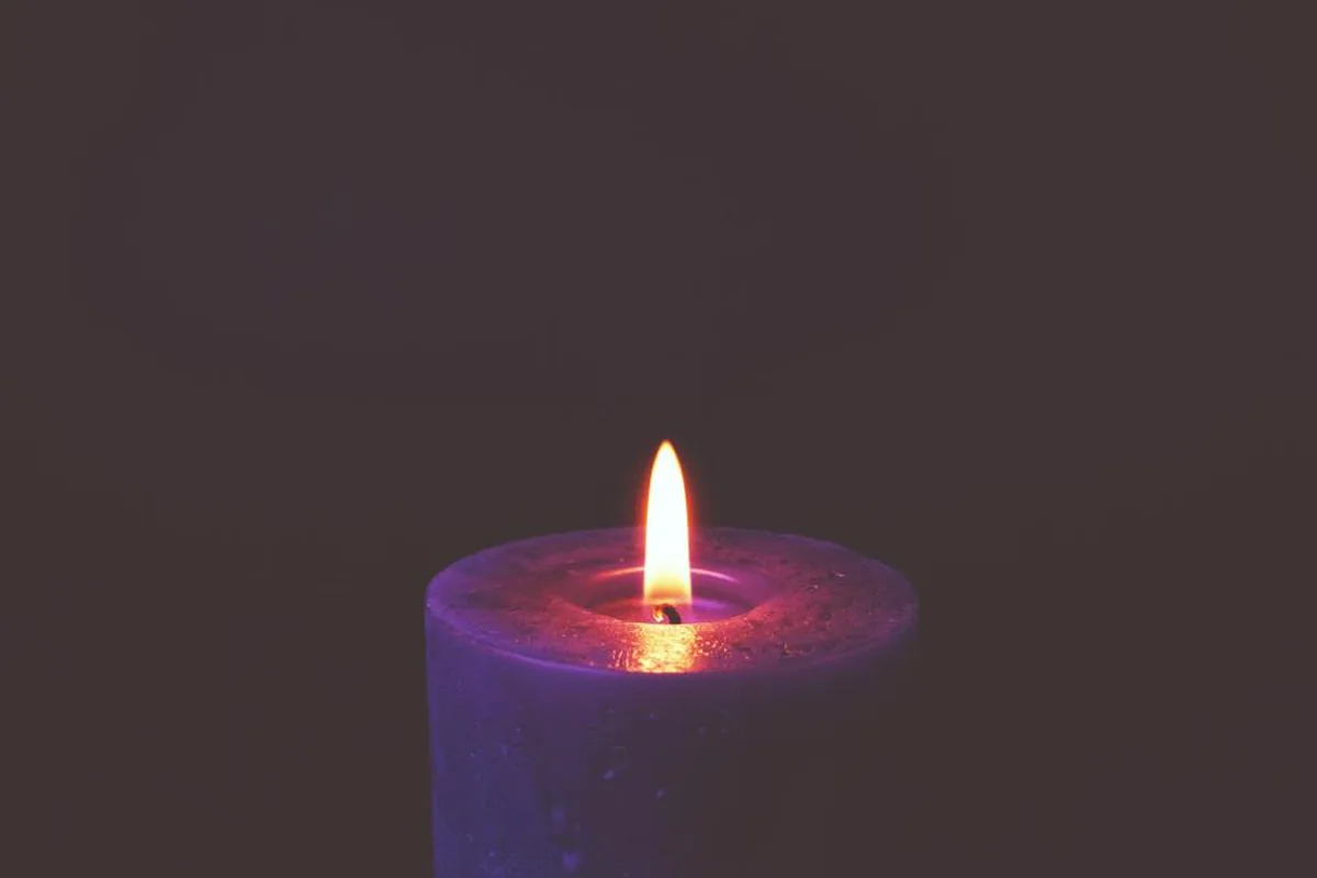 Una vela gruesa de color violeta encendida sobre un fondo oscuro y liso