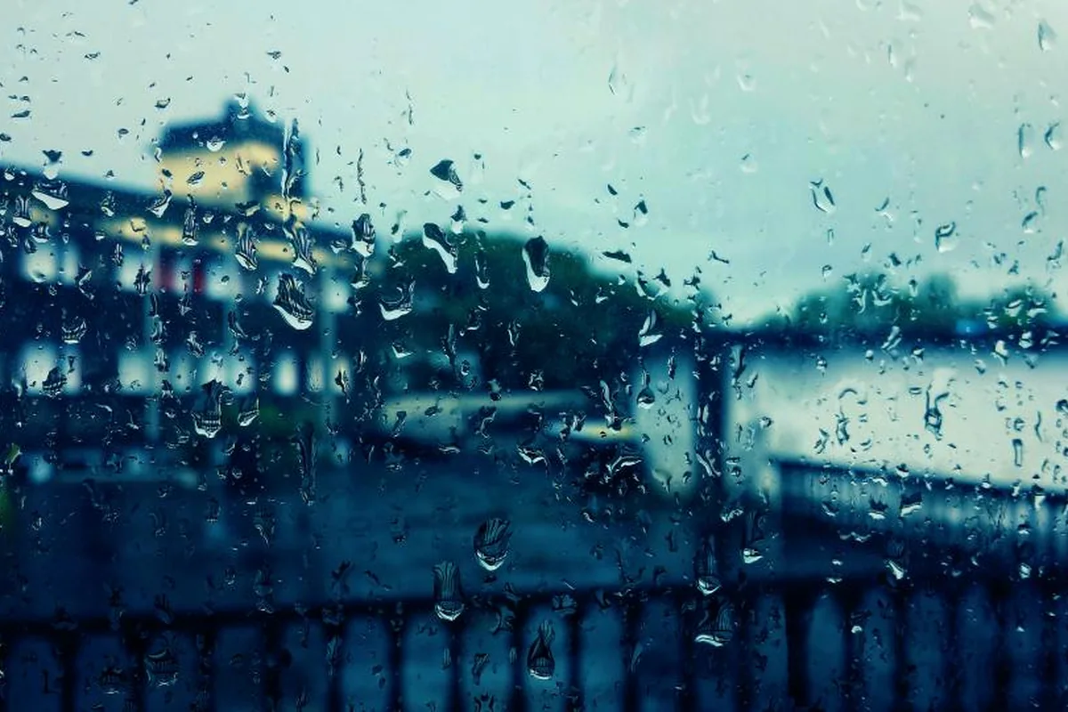 Cristal de una ventana cubierto de gotas de lluvia con edificios desenfocados al fondo en una tarde gris