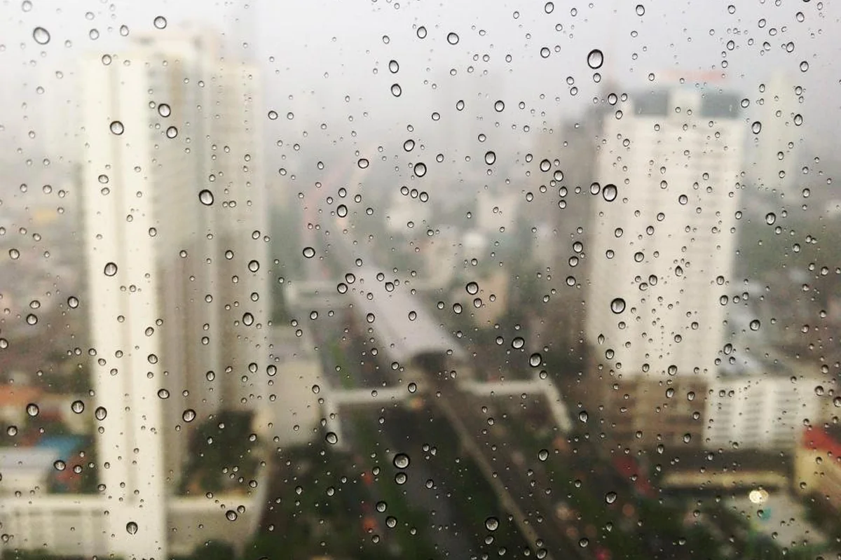Cristal de una ventana cubierto de gotas de lluvia con edificios altos y una avenida desenfocados al fondo