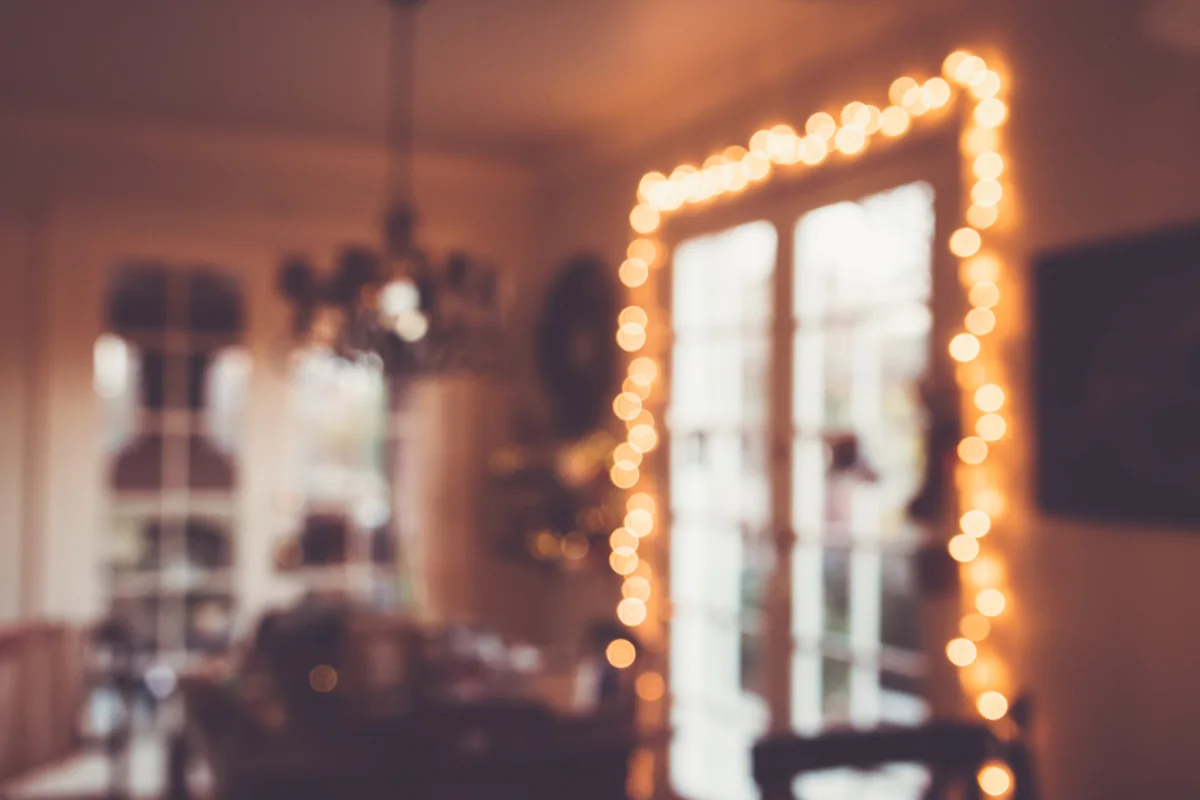 Salón desenfocado con una ventana rodeada de una guirnalda de luces cálidas y una lámpara de techo