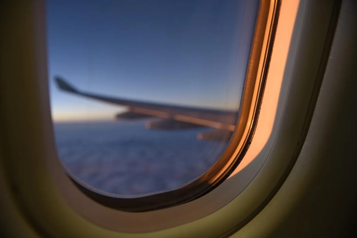 Ventanilla de avión con el ala desenfocada sobre un manto de nubes y el cielo azul oscuro al atardecer