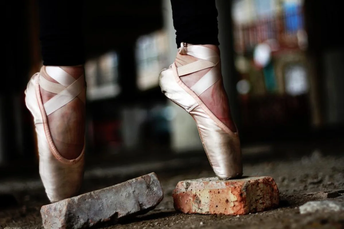 Pies de una bailarina con zapatillas de puntas de ballet apoyados sobre dos ladrillos en un suelo de tierra